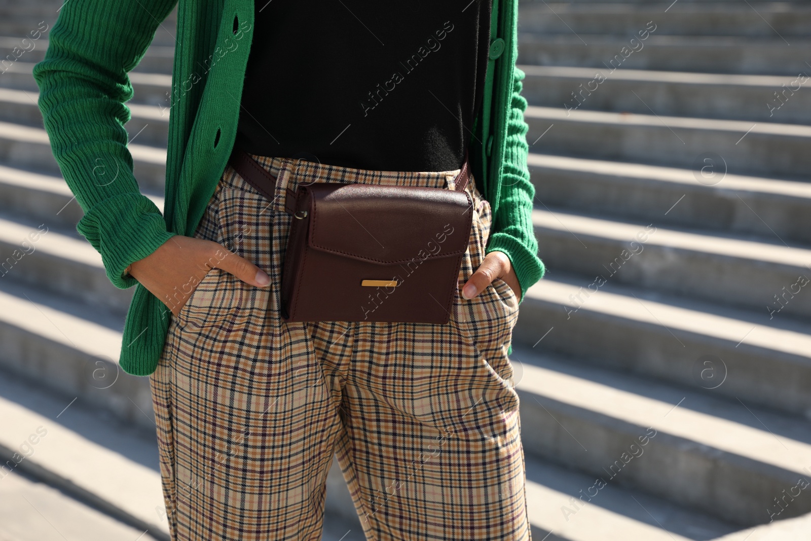 Photo of Young African American woman with stylish waist bag on stairs outdoors, closeup