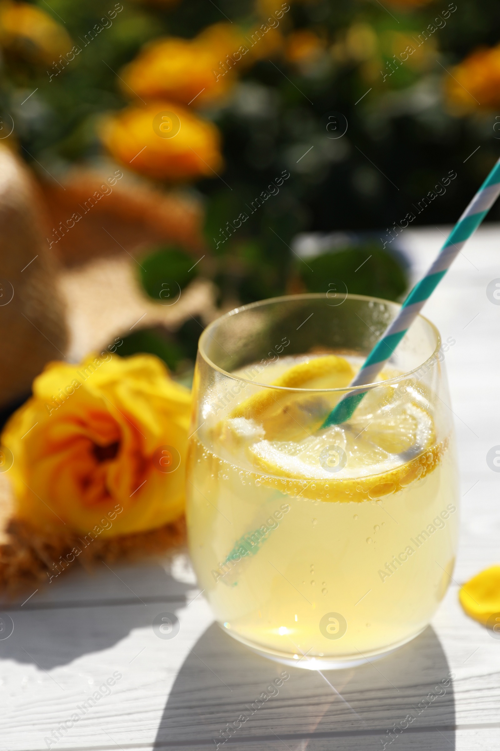 Photo of Composition with glass of refreshing lemonade and beautiful rose on white wooden table in blooming garden