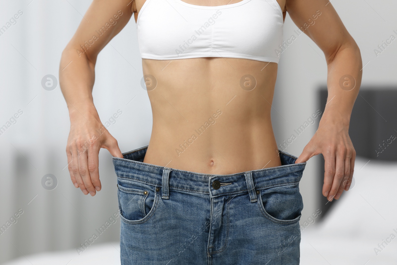 Photo of Slim woman wearing big jeans at home, closeup. Weight loss