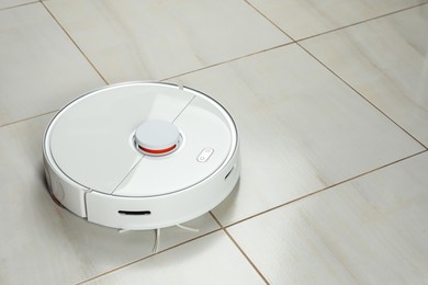Photo of Robotic vacuum cleaner on white tiled floor, space for text