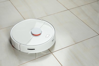 Robotic vacuum cleaner on white tiled floor, space for text