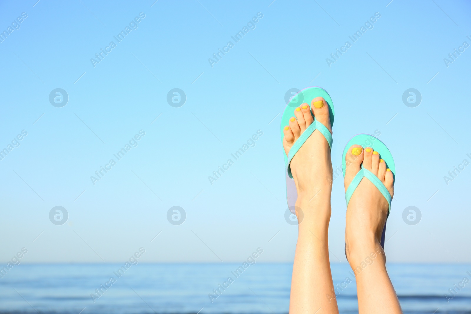 Photo of Closeup of woman wearing flip flops near sea, space for text. Beach accessories