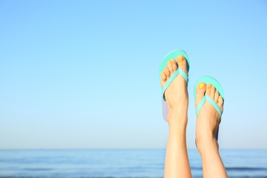 Photo of Closeup of woman wearing flip flops near sea, space for text. Beach accessories