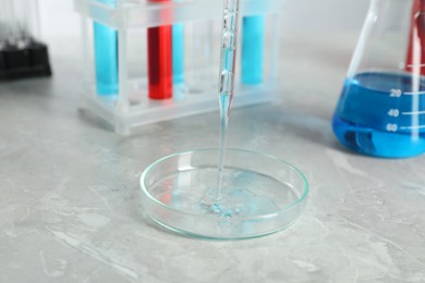 Photo of Dripping liquid from pipette into petri dish at grey marble table, closeup