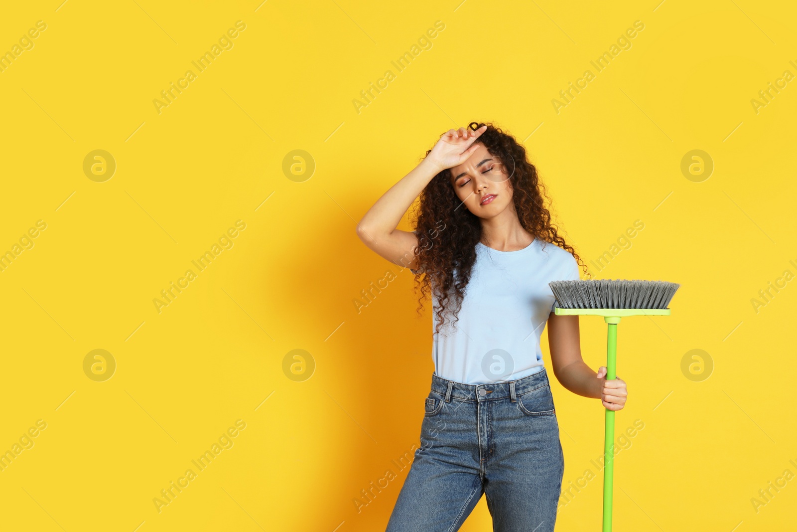 Photo of Tired African American woman with green broom on orange background, space for text