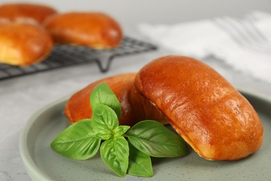 Photo of Delicious baked pirozhki and basil on light grey table, closeup