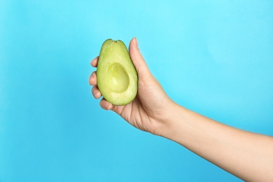 Woman holding ripe cut avocado on color background