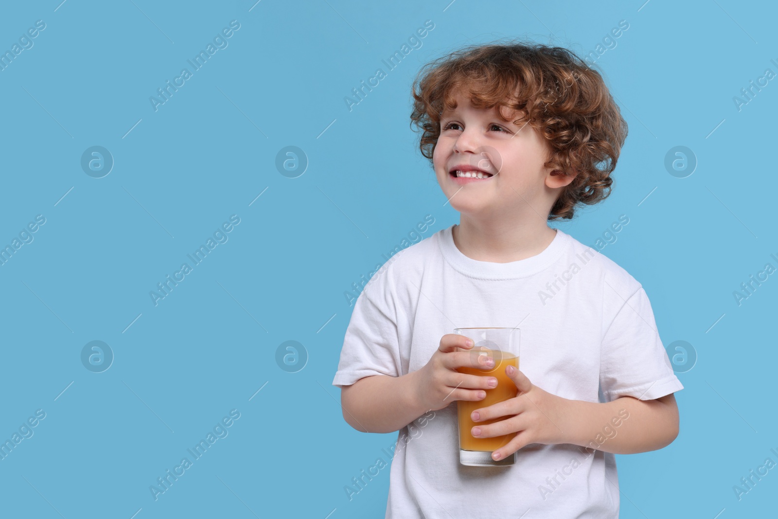 Photo of Cute little boy with glass of fresh juice on light blue background, space for text