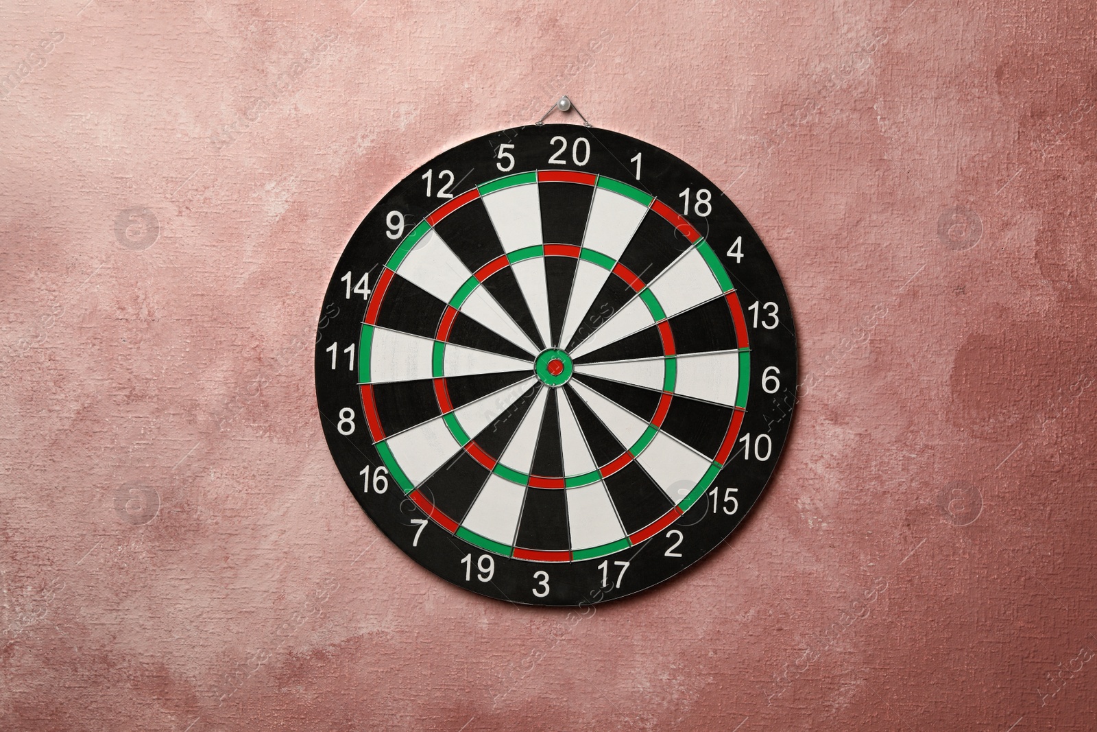 Photo of Dart board hanging on pink textured wall