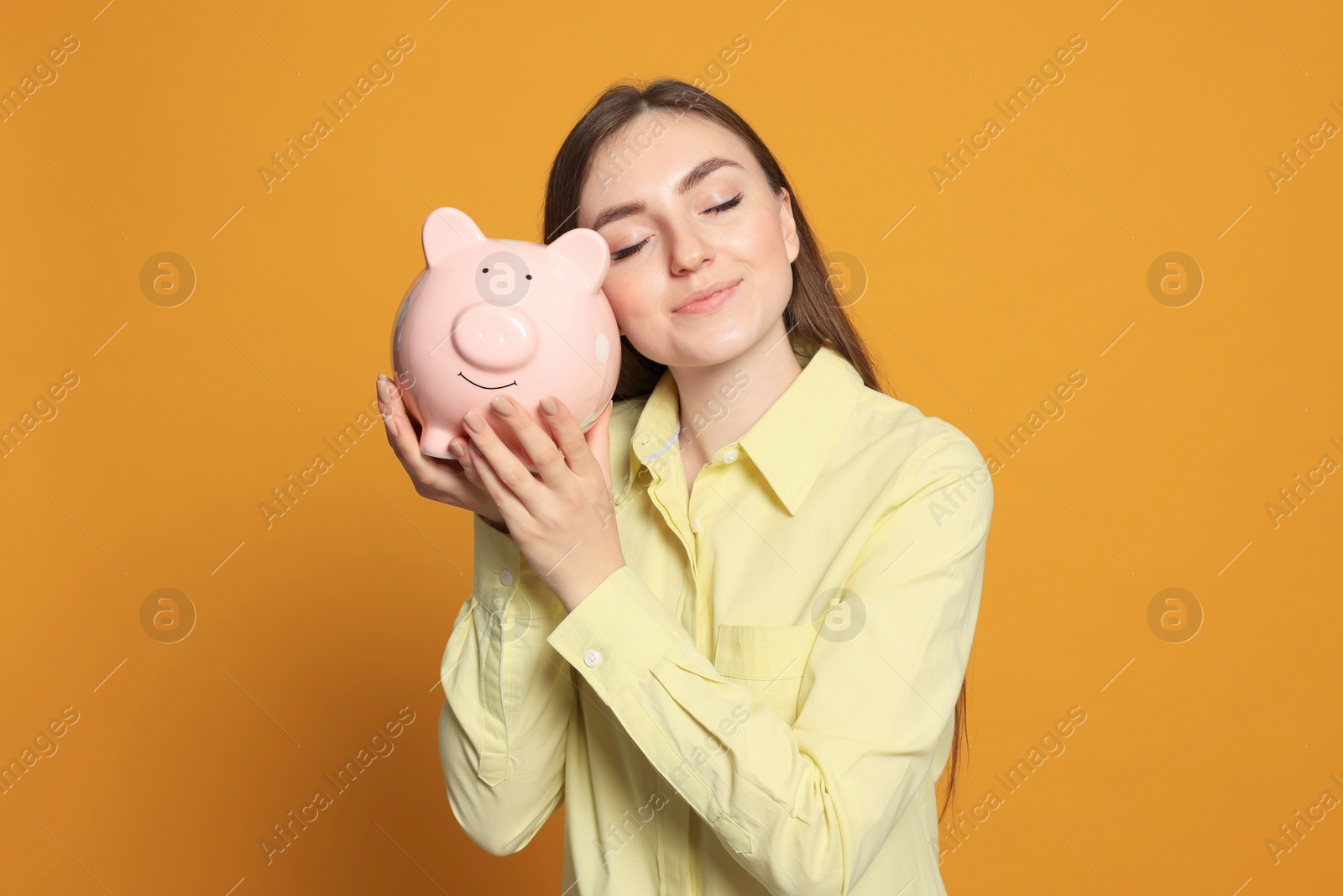 Photo of Happy young woman with piggy bank on orange background