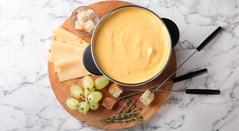 Flat lay composition with pot of delicious cheese fondue on white marble table. Banner design