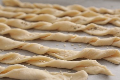 Photo of Homemade breadsticks with sesame on baking sheet, closeup. Cooking traditional grissini