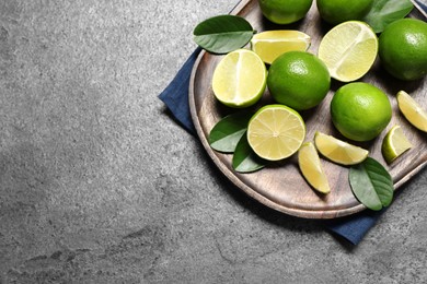 Fresh ripe limes and leaves on grey table, top view. Space for text