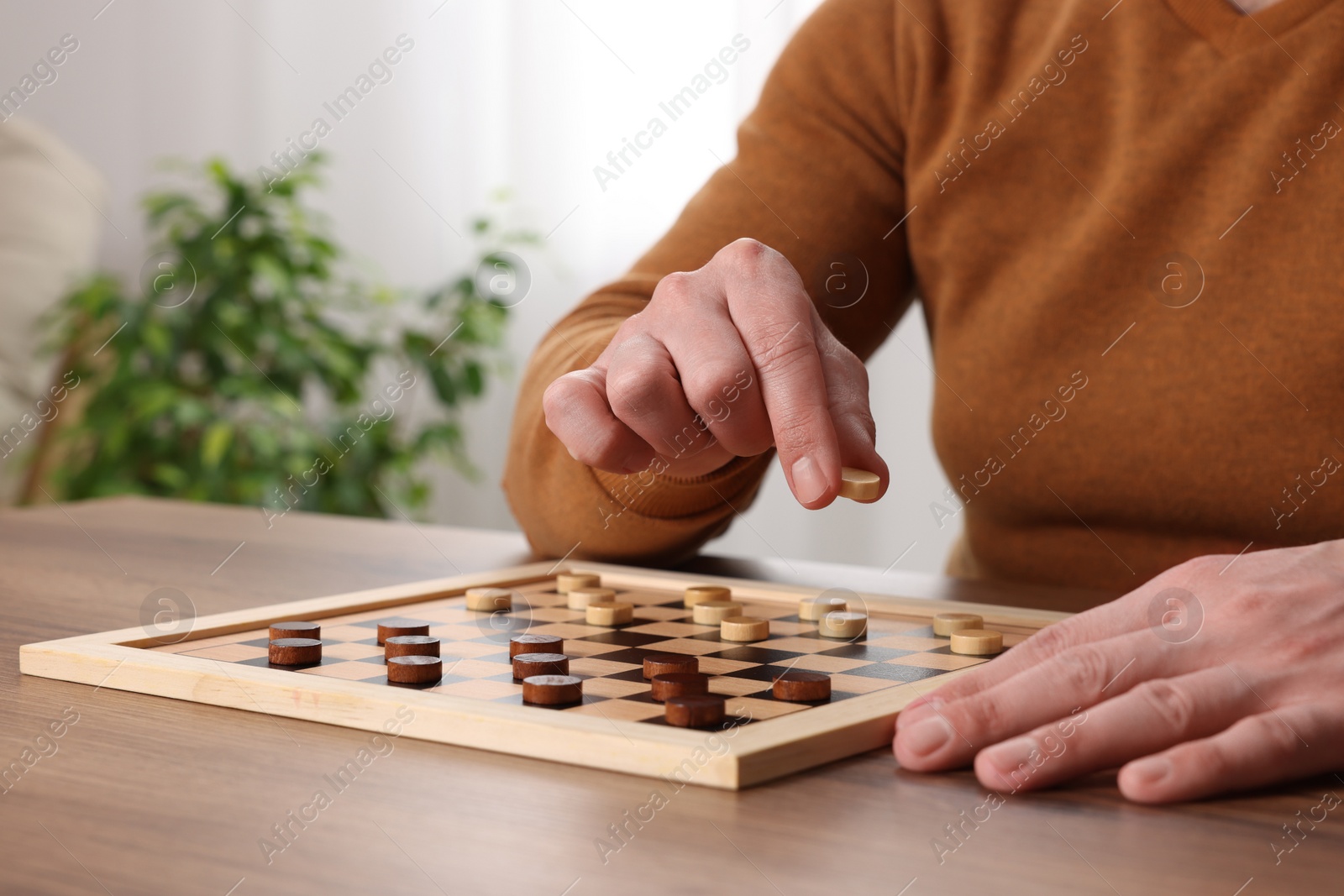 Photo of Playing checkers. Man thinking about next move at table in room, closeup