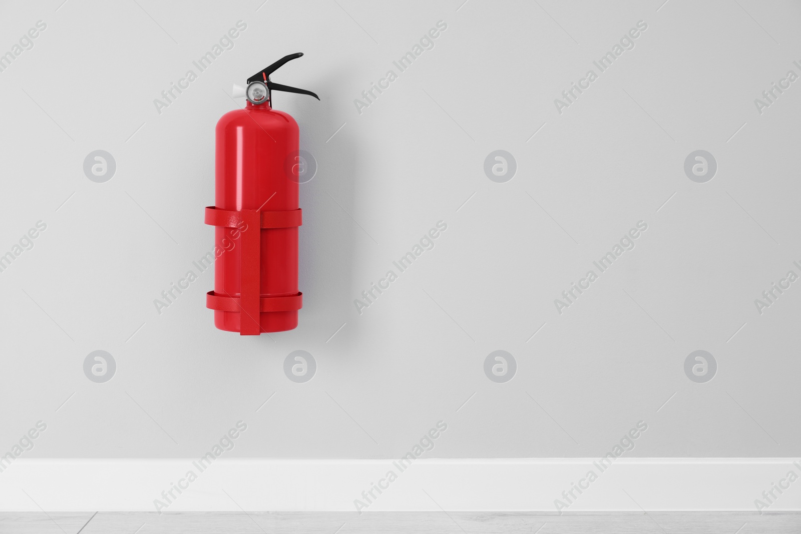 Photo of Fire extinguisher on light grey wall, space for text