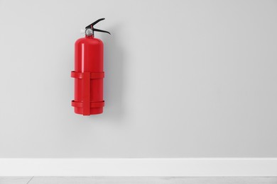 Photo of Fire extinguisher on light grey wall, space for text