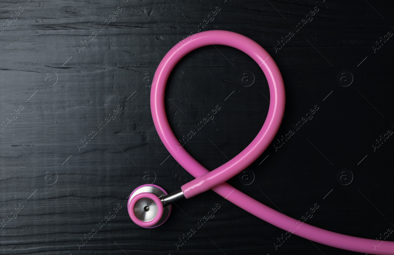 Photo of Pink stethoscope folded like awareness ribbon on wooden background, top view. Breast cancer concept