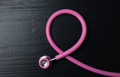 Pink stethoscope folded like awareness ribbon on wooden background, top view. Breast cancer concept