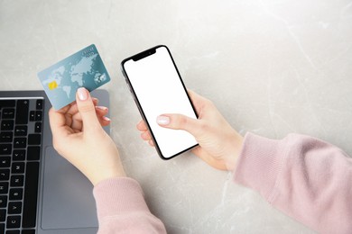 Online payment. Woman using credit card and smartphone with blank screen near laptop at light grey table, top view