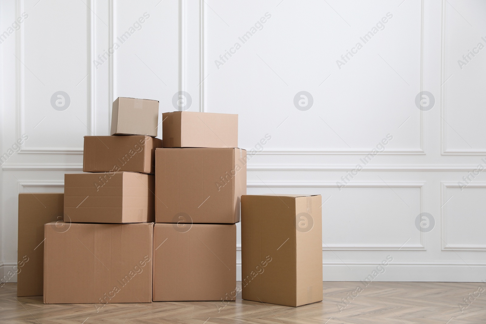 Photo of Heap of cardboard boxes near white wall indoors, space for text. Moving day