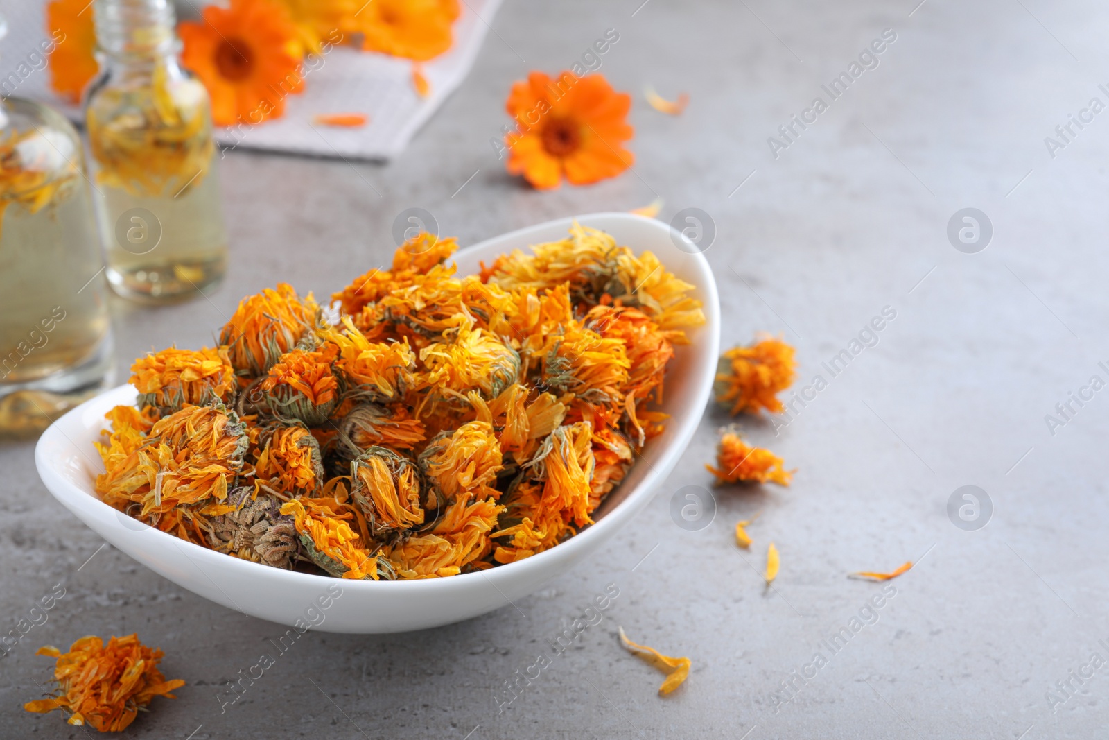 Photo of Plate of dry calendula flowers on light grey table. Space for text