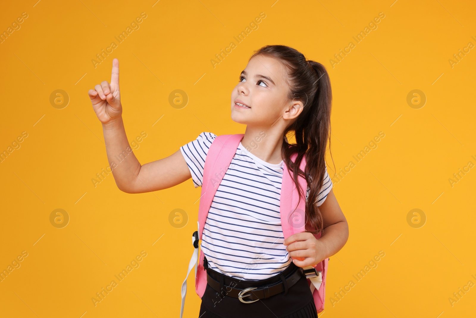 Photo of Cute schoolgirl pointing upwards on orange background