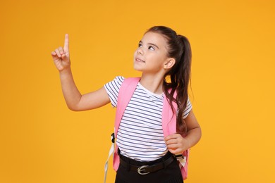 Cute schoolgirl pointing upwards on orange background