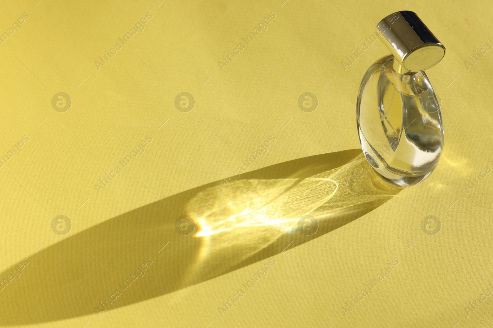 Photo of Luxury women's perfume. Sunlit glass bottle on yellow background. Space for text