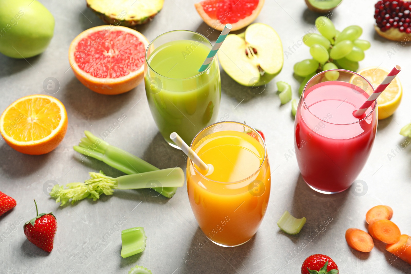 Photo of Three glasses of different juices and fresh ingredients on light background