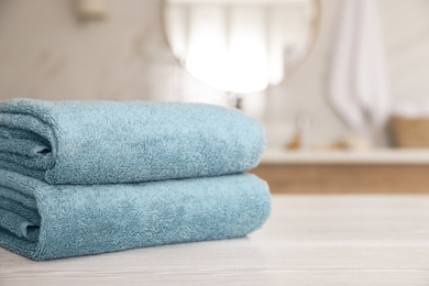 Stack of clean towels on white wooden table in bathroom. Space for text