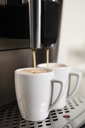 Photo of Espresso machine pouring coffee into cups against blurred background, closeup