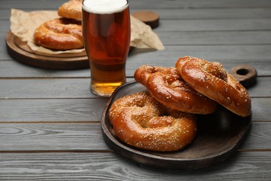 Photo of Tasty freshly baked pretzels and glass of beer on grey wooden table. Space for text
