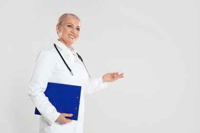 Photo of Mature doctor with clipboard on light grey background. Space for text