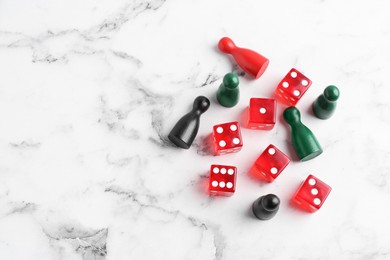 Red dices and game pieces on white marble table, flat lay. Space for text