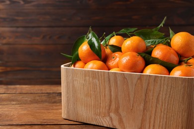 Fresh tangerines with green leaves in crate on wooden table, closeup. Space for text