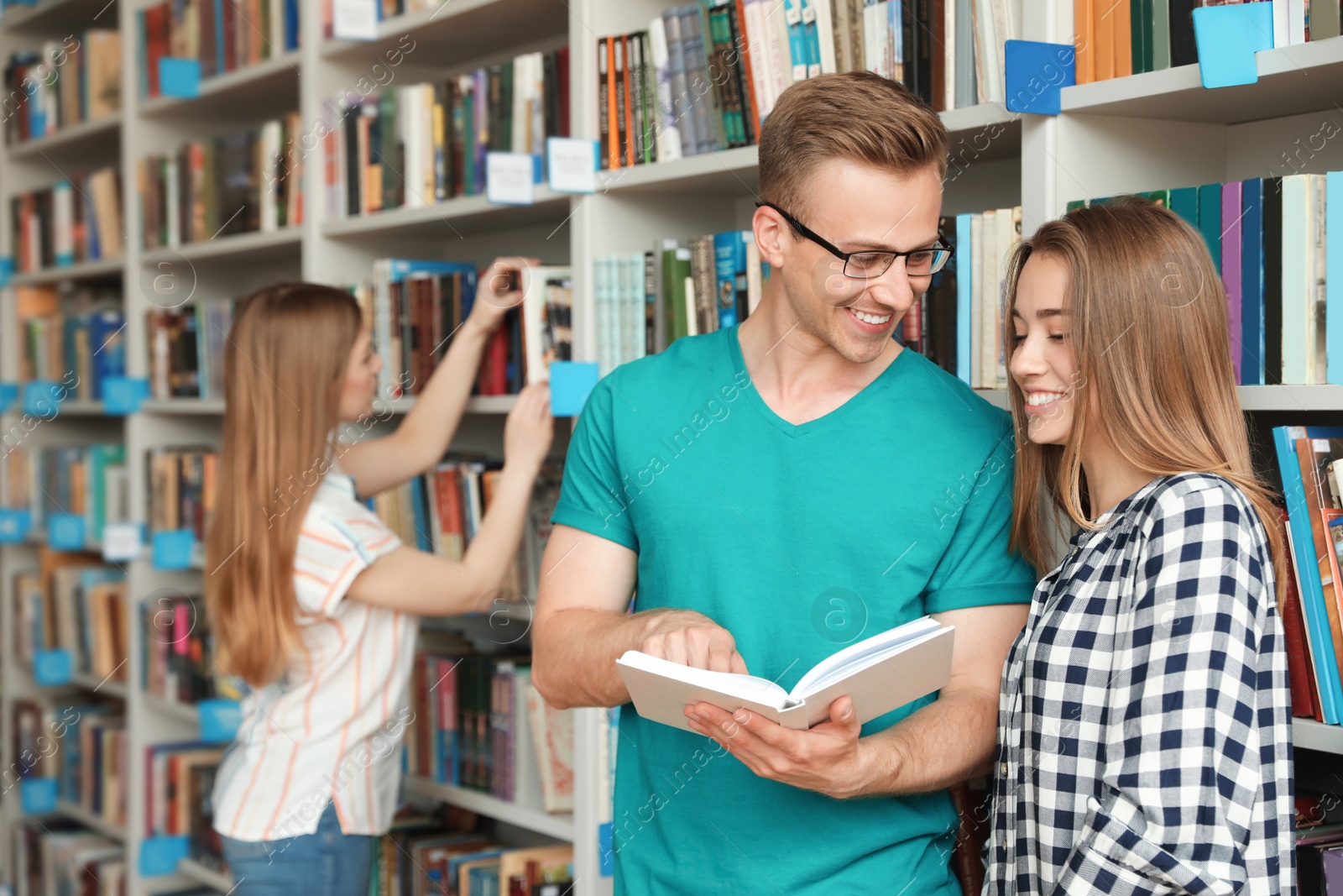 Photo of Young people standing near bookshelves in library