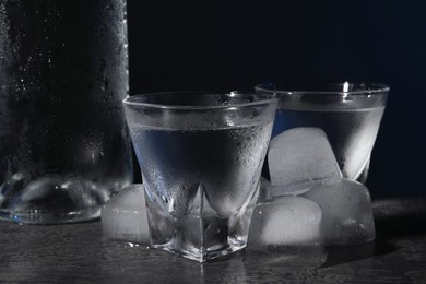 Photo of Vodka in shot glasses with ice on black table against dark background, closeup