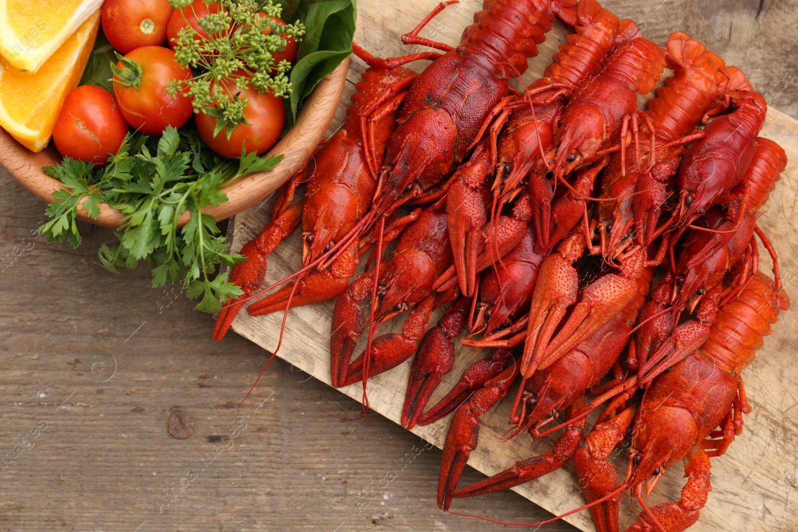 Photo of Delicious red boiled crayfish and products in bowl on wooden table, top view