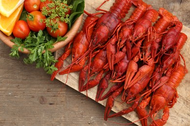 Delicious red boiled crayfish and products in bowl on wooden table, top view