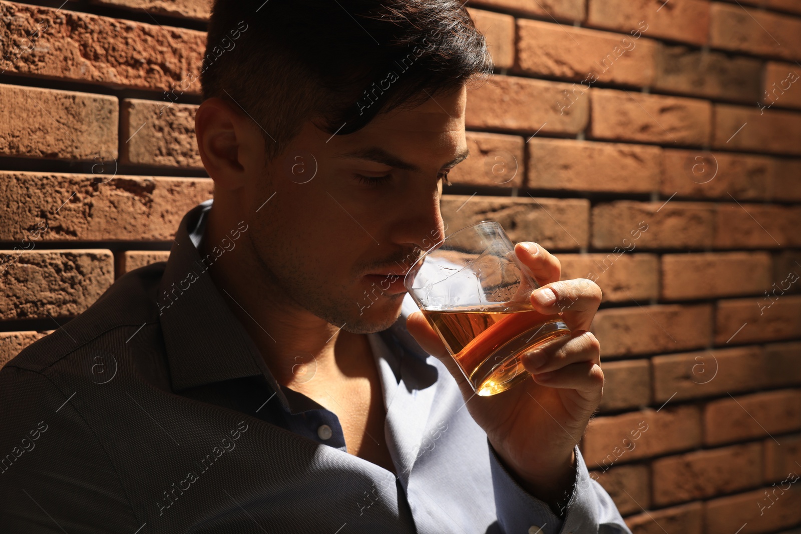 Photo of Addicted man drinking alcohol near red brick wall