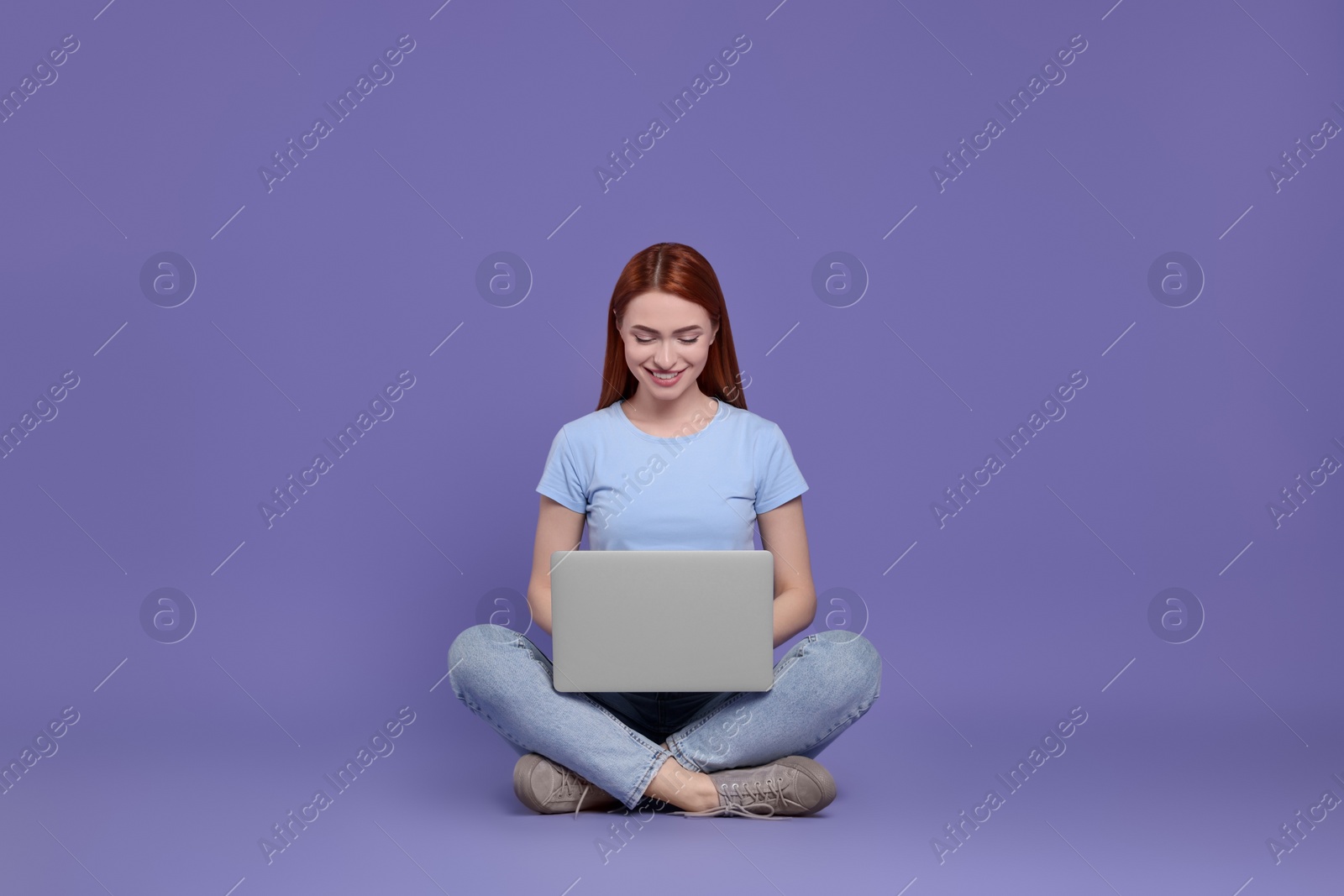 Photo of Smiling young woman working with laptop on lilac background