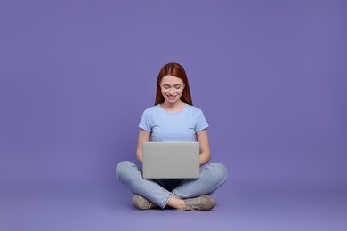 Smiling young woman working with laptop on lilac background