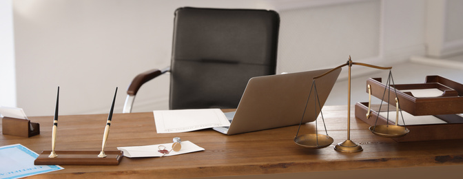 Scales of justice, laptop and wax stamp on desk in lawyer's office. Banner design