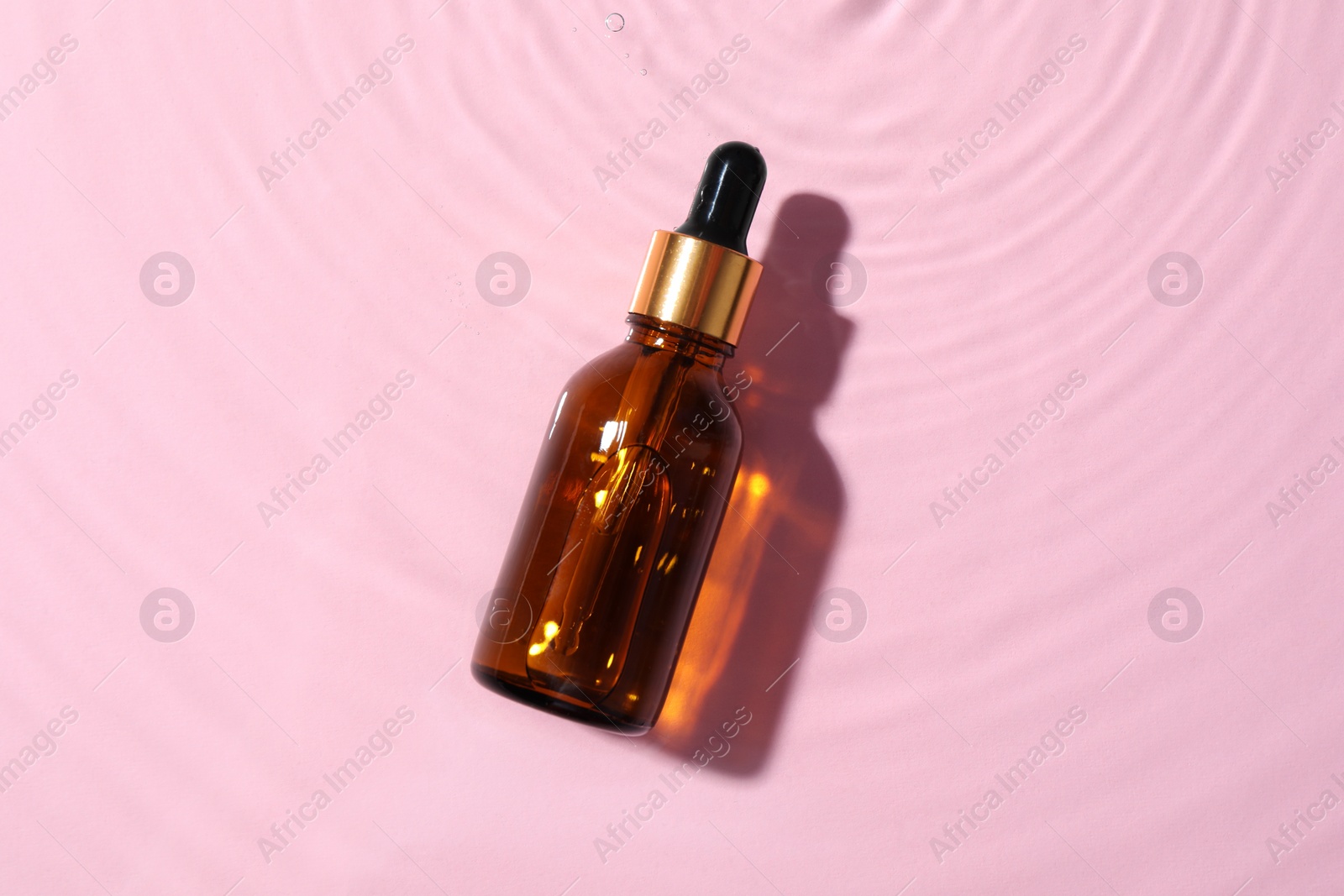 Photo of Bottle of cosmetic oil in water on pink background, top view