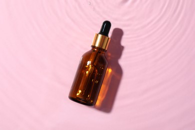 Bottle of cosmetic oil in water on pink background, top view
