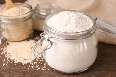 Photo of Jars with quinoa flour and seeds on wooden table, closeup