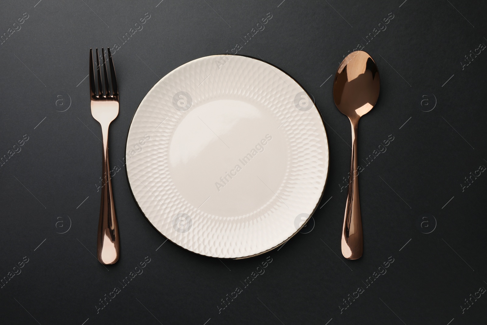 Photo of Empty plate, golden fork and spoon on black table, top view