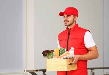 Food delivery courier holding wooden crate with products indoors. Space for text