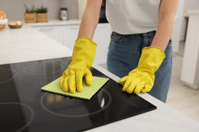 Woman with spray bottle and microfiber cloth cleaning electric stove in kitchen, closeup