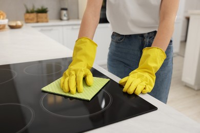 Photo of Woman with spray bottle and microfiber cloth cleaning electric stove in kitchen, closeup